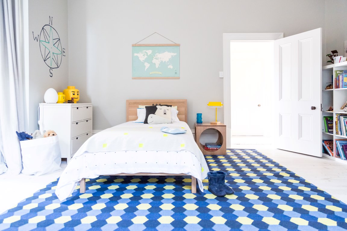 اتاق کودک پسر مدرن و شیک با تخت خواب چوبی و فرش آبی که دیوار آن نقشه جهان و نقاشی قطب نما دارد
